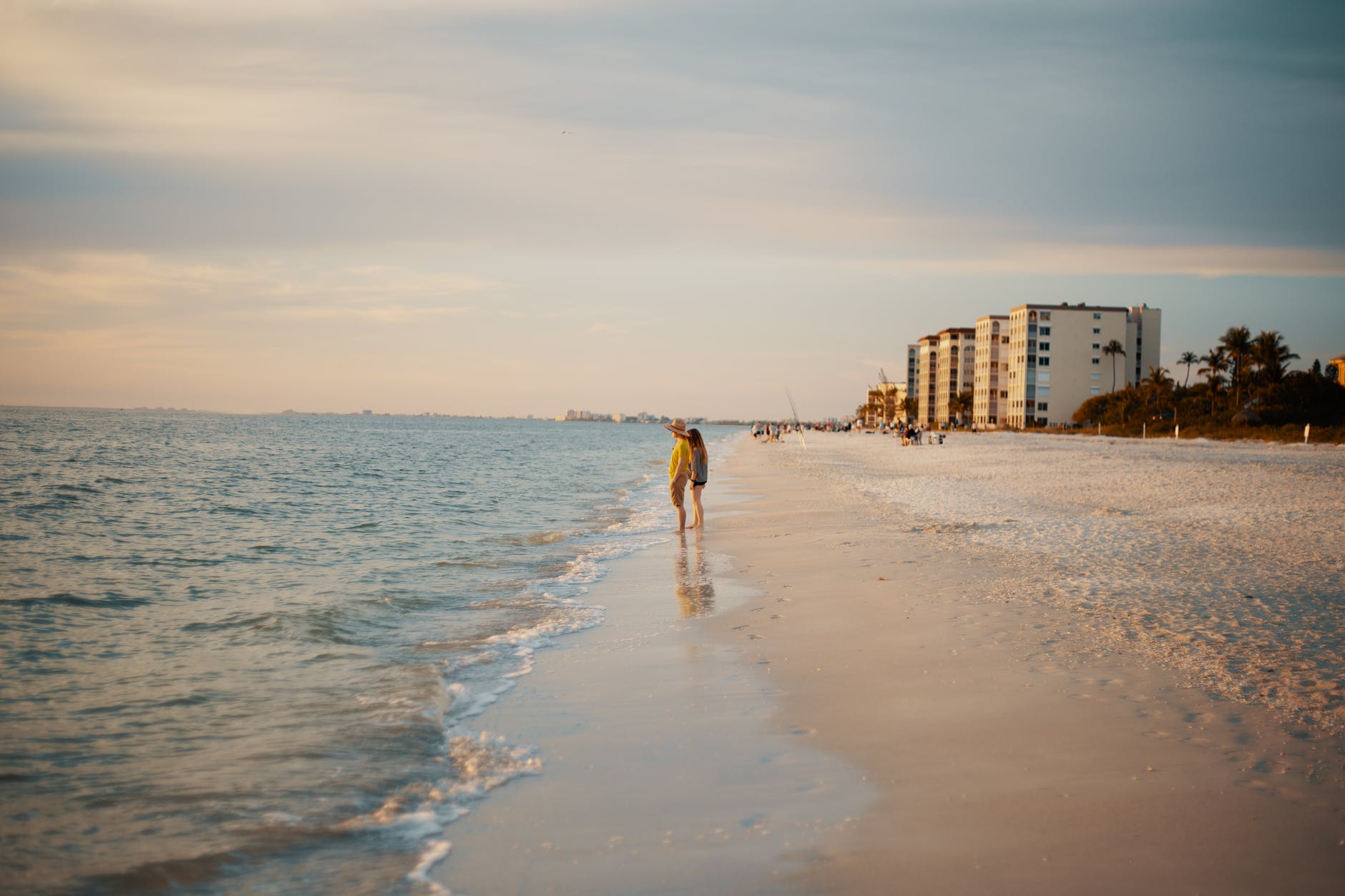 anonymous couple standing on sandy seashore at sundown