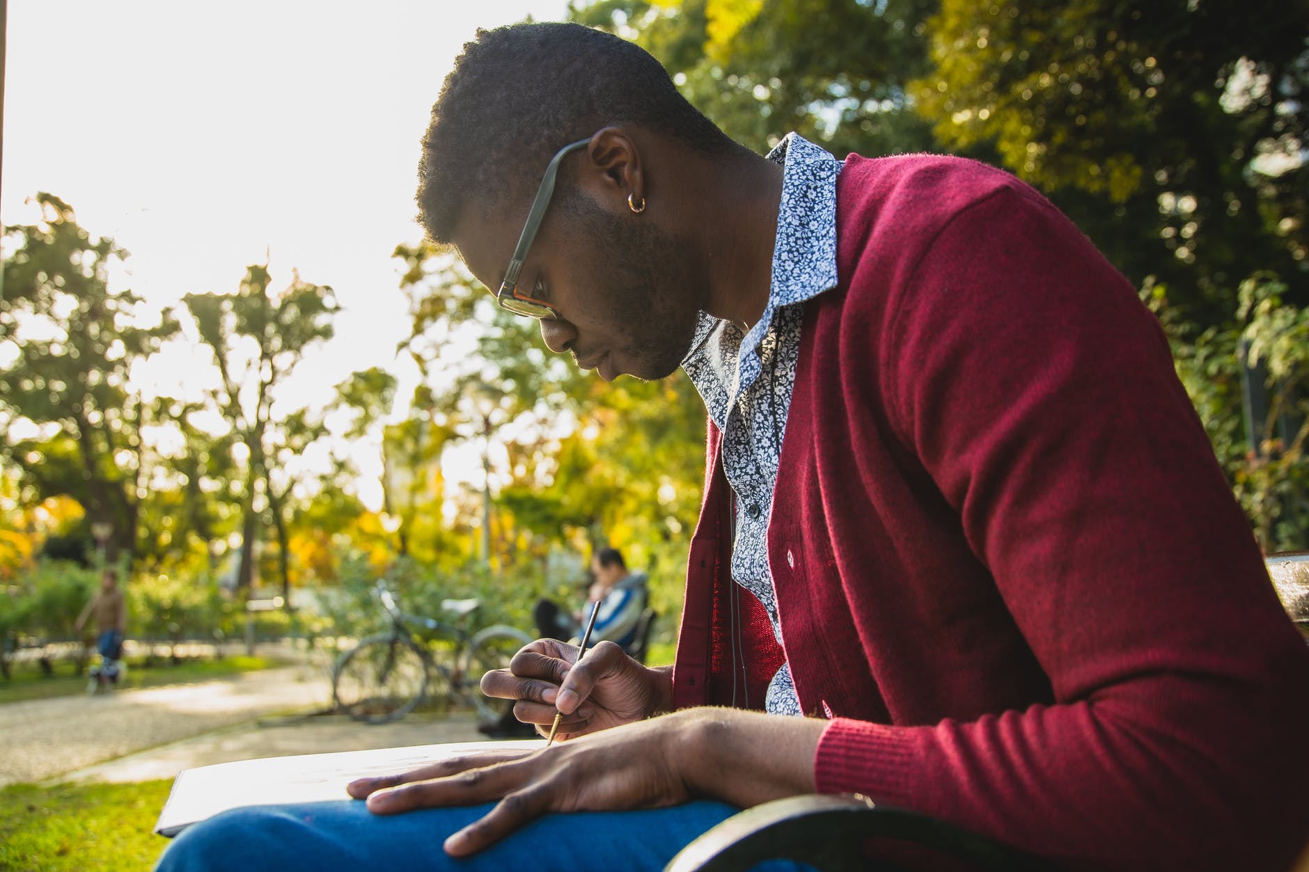 black student writing on paper while studying in park