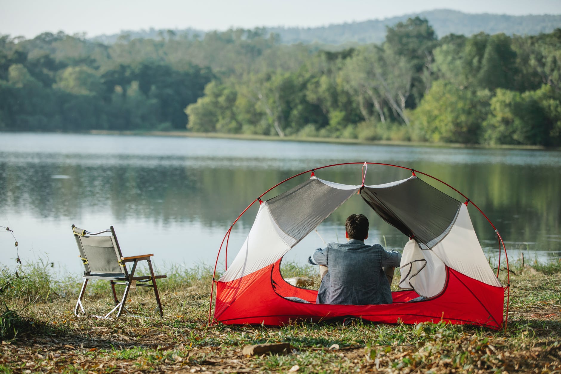 anonymous hiker contemplating river and trees from tent