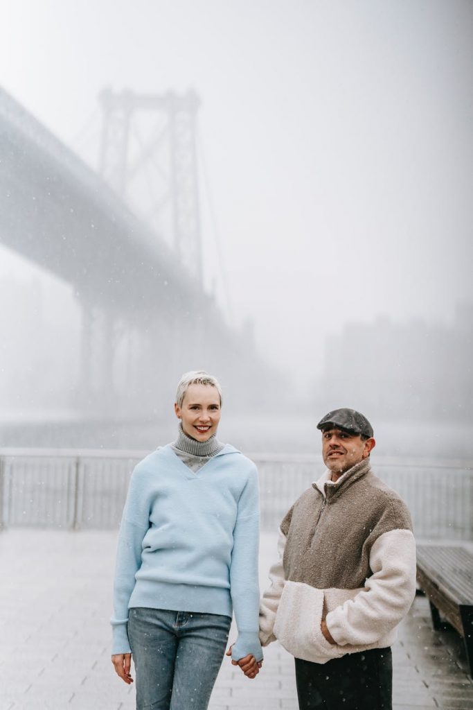 smiling couple on embankment against bridge in foggy town