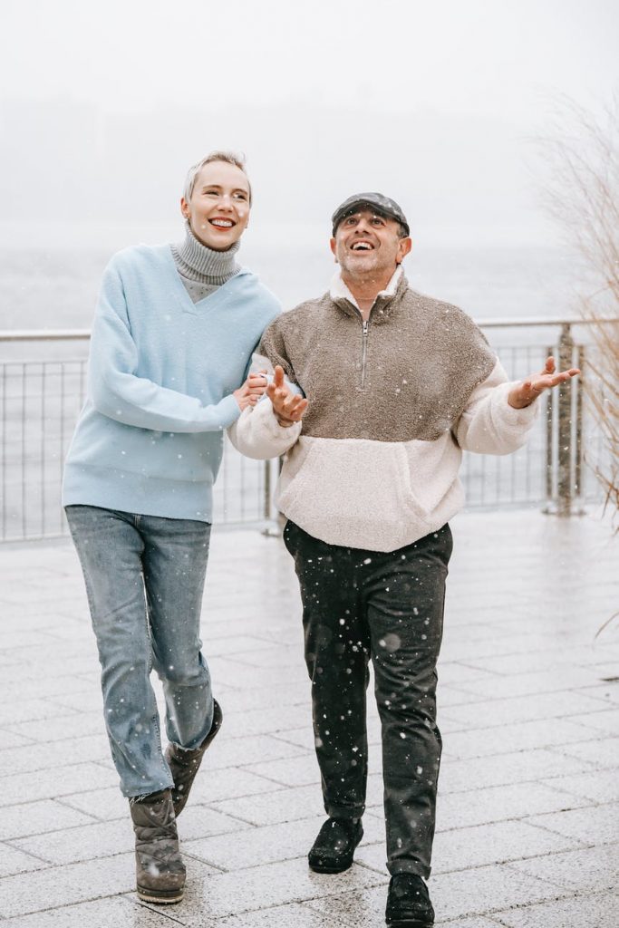 happy couple admiring snowfall on city embankment