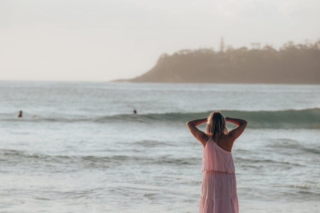 female in pink dress standing near sea in sunny day