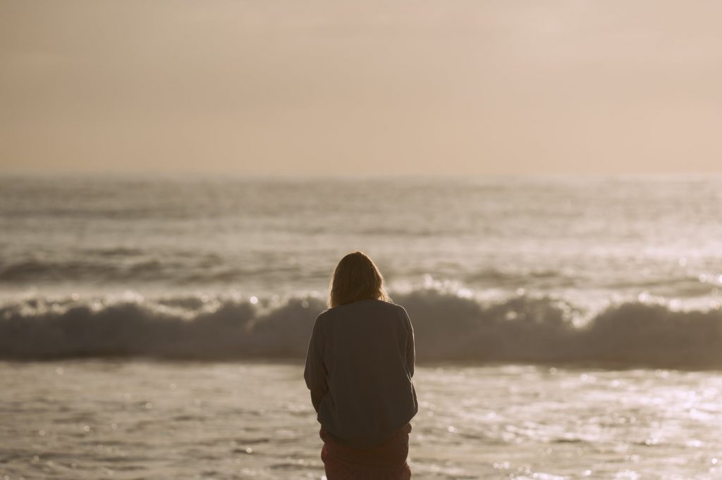 person standing on shore and admiring wavy ocean in sunlight