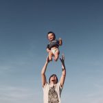 photo of man in raising baby under blue sky