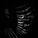 black man in striped shadows in darkness